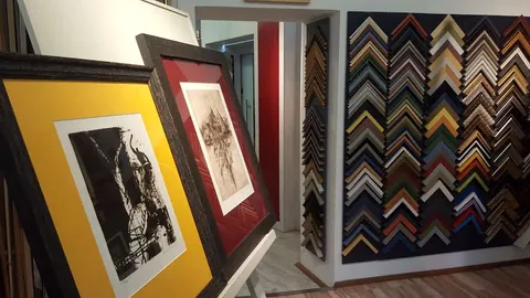 Zwei Grafiken mit gelbem und bordeauxrotem Passepartout vor der Musterwand mit Rahmenecken