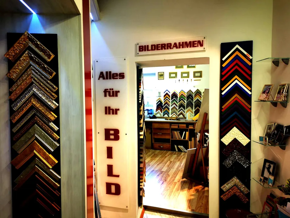 Eingang zur Bilderrahmenwerkstatt mit Schriftzug „Alles für Ihr Bild“ und Rahmenmustern