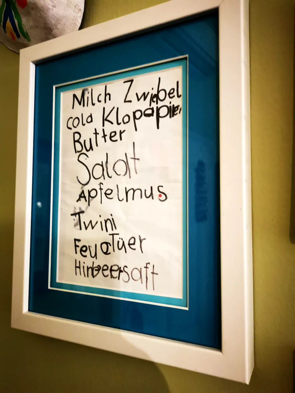 Gerahmter Einkaufszettel eines Kindes in weißem Rahmen mit blauem Passepartout